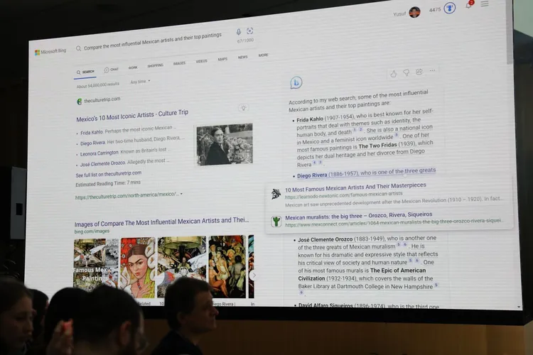 Telão exibindo a busca do Bing com a pergunta sobre os artistas mexicanos mais influentes, com resposta gerada pelo chat e miniaturas de pinturas, diante de pl…