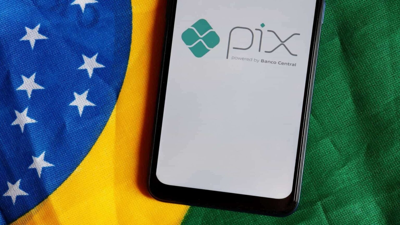 Smartphone com a logomarca do Pix, sistema de pagamentos do Banco Central, sobre uma bandeira do Brasil