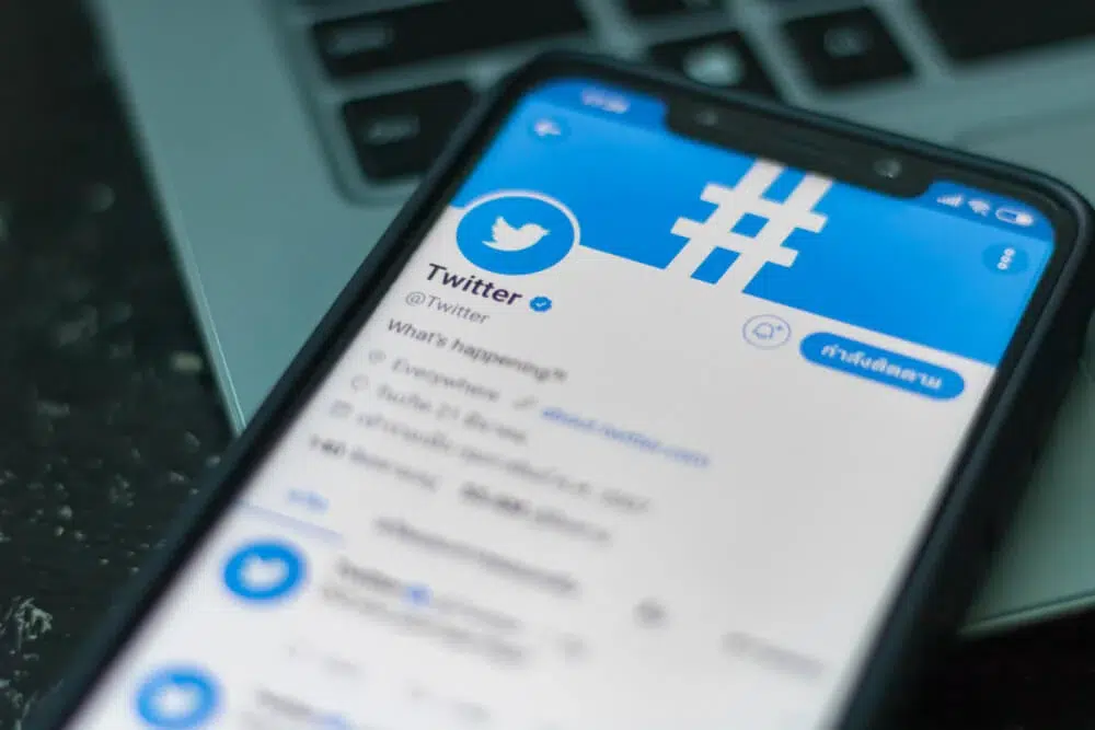 Smartphone exibindo o perfil oficial do Twitter, com o logo azul e o selo de verificação, sobre um teclado de notebook
