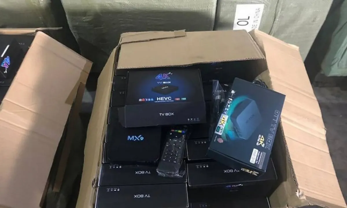 Caixas de papelão abertas com aparelhos TV box apreendidos, incluindo modelos MXQ e HEVC 4K, sendo um deles com controle remoto