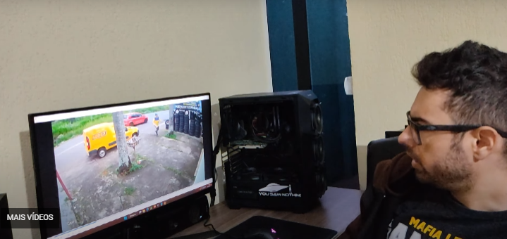 Homem de óculos assiste a vídeo de câmera de segurança em monitor ao lado de um PC gamer com case preto e vidro lateral