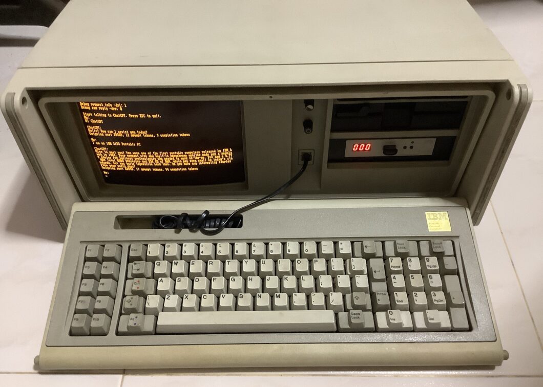 Computador portátil IBM 5155 dos anos 80 com tela de fósforo laranja exibindo texto de terminal DOS rodando o ChatGPT