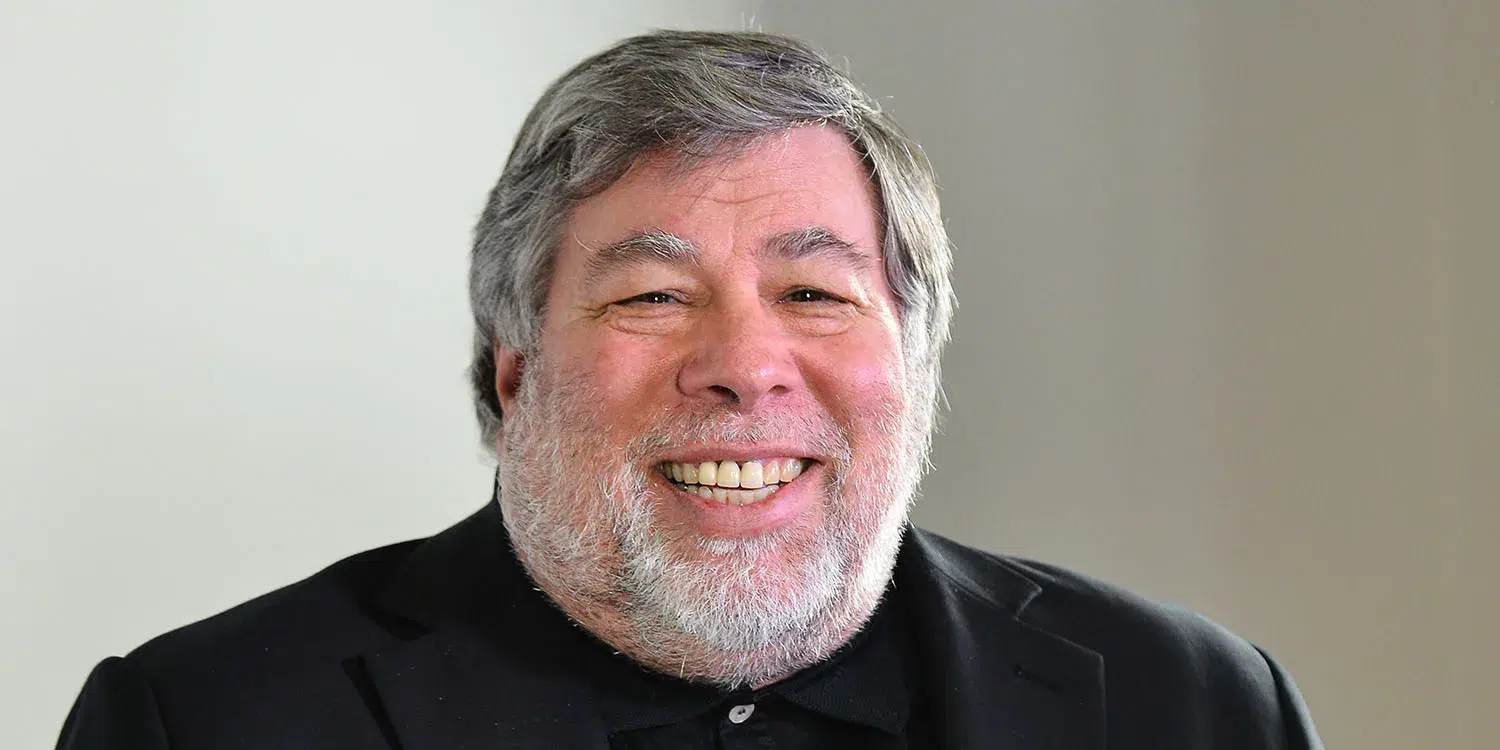 Homem de cabelo grisalho e barba branca, sorrindo, vestindo camisa escura, em fundo claro e desfocado