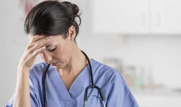Profissional de saúde de uniforme azul com estetoscópio no pescoço, com a mão na testa e expressão cansada, em ambiente hospitalar